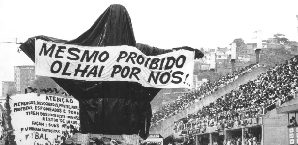 Carro "Cristo Mendigo" da escola de samba Beija-Flor de Nilópolis, envolto em plástico preto e com uma faixa com a inscrição "Mesmo proibido, olhai por nós!", durante o desfile no sambódromo do Rio de Janeiro (7/2/1989)